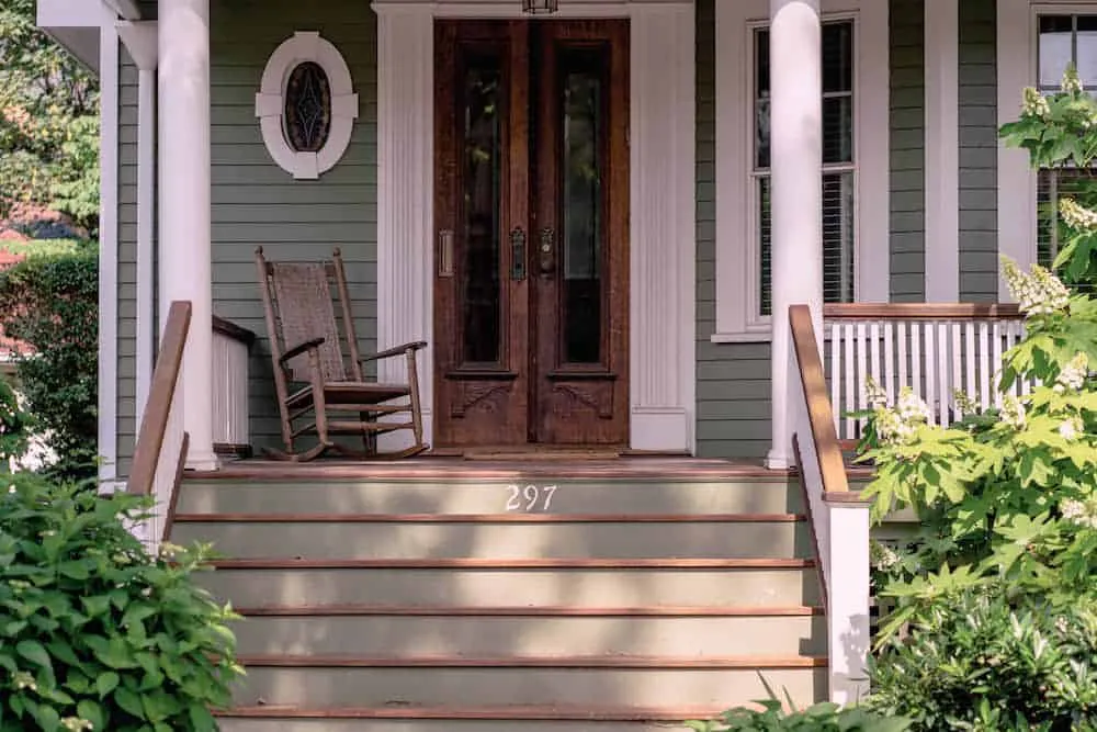 A wooden front door and porch with a rocking chair and steps