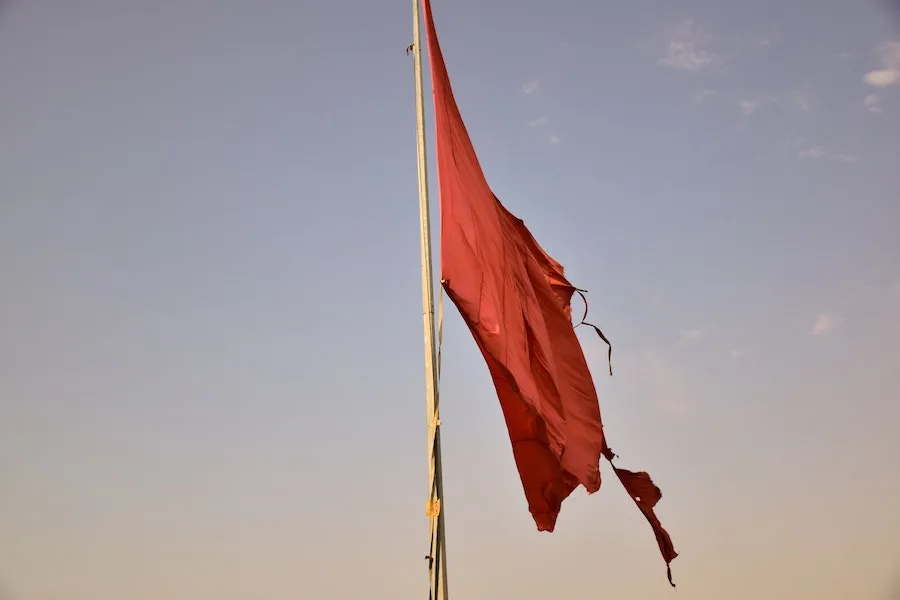 A tattered red flag flying against a pale sky.