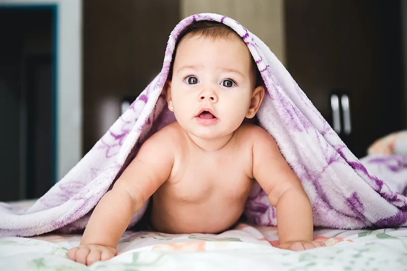A baby peeking out from under a purple blanket.