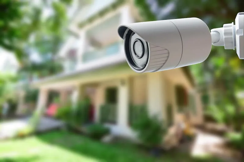 A white CCTV security camera mounted in front of a house with a garden