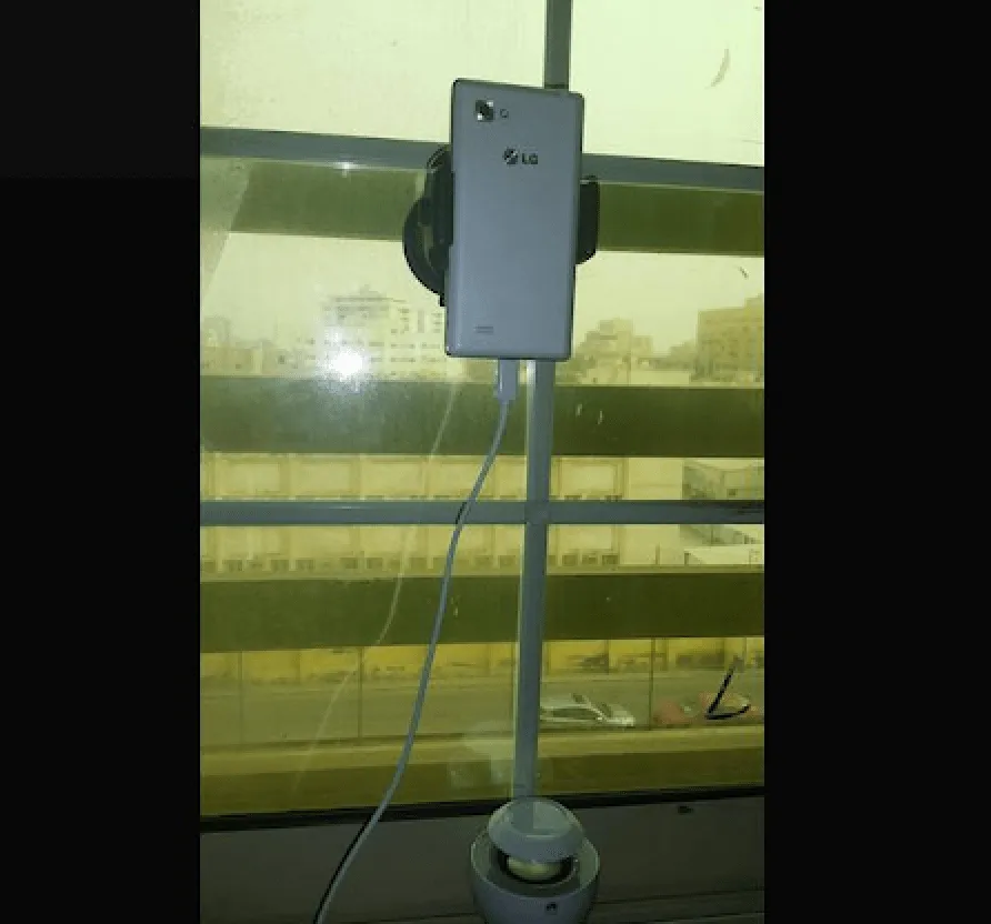 A phone held in a cradle on a tall stand next to a window.
