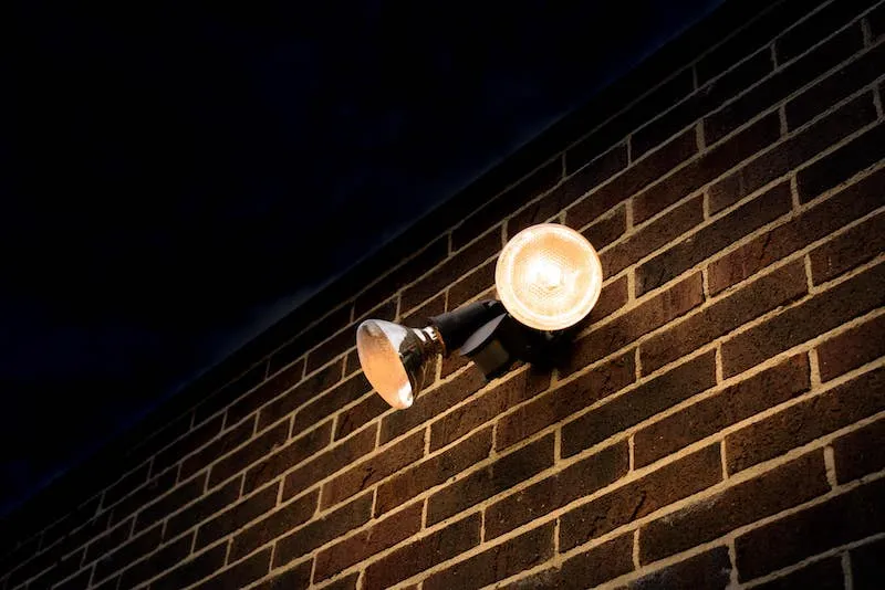 A two-lamp outdoor floodlight lit up at night on a brick wall