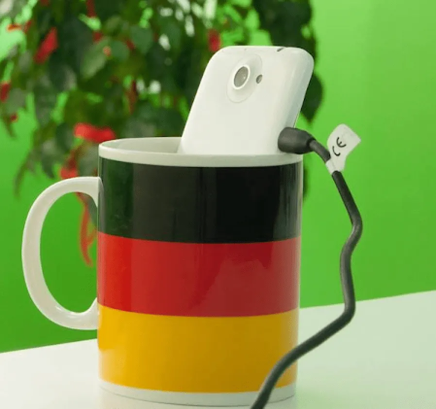 A white phone standing in a striped mug with a charging cable, only the top of the phone showing.