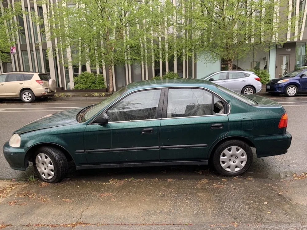 a green car parked on the street has been broken in through a smashed window