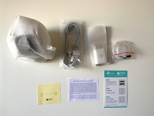 The contents included with Kasa Spot Pan Tilt: the camera, micro USB cable, charger, Quick Start guide, screws with wall mounts, and alignment/mounting stickers