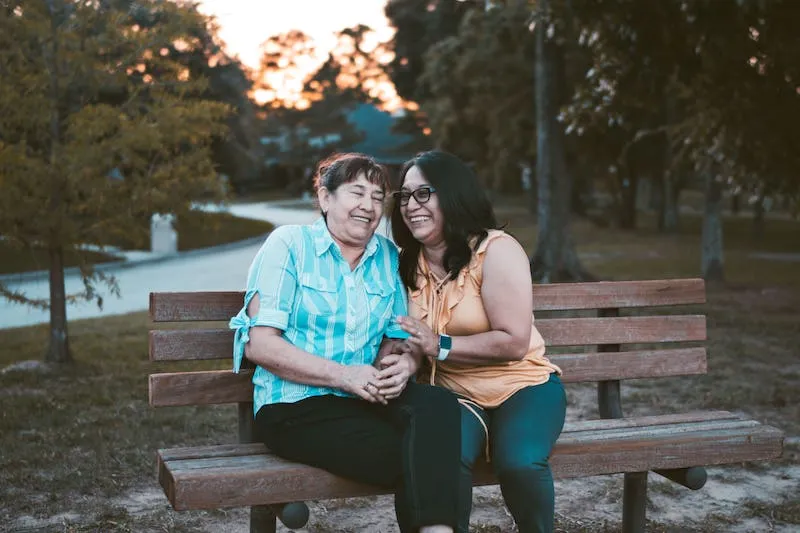 Two middle-aged women laugh together on a park bench