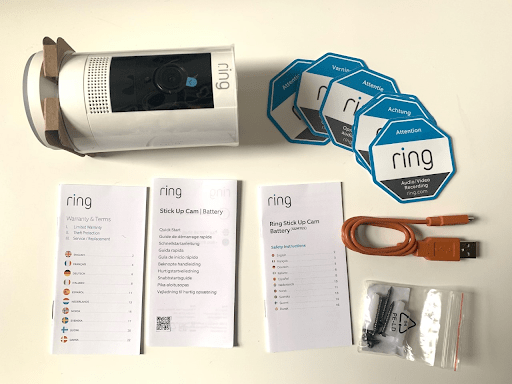 Ring Stick Up Cam (Battery) contents: camera, warning stickers, three instruction manuals, a micro USB charger, and screws and wall plugs.
