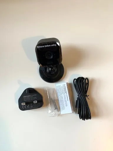 The contents of the Blink Mini box, including the Blink Mini security camera, plug, screws x 2, safety information, and micro USB cable.