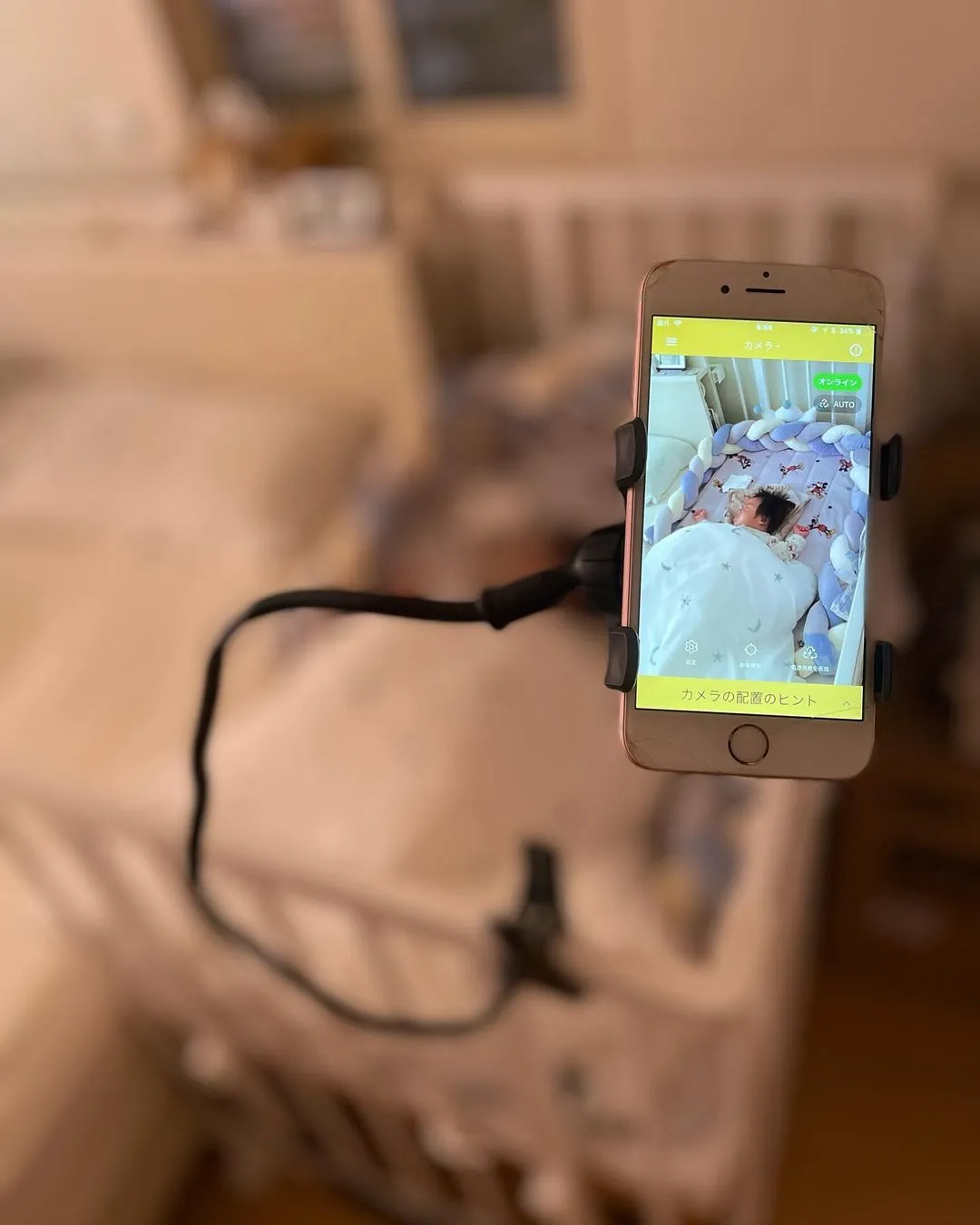 An old phone on a flexible arm stand used as a baby monitor, showing a sleeping baby in a crib.