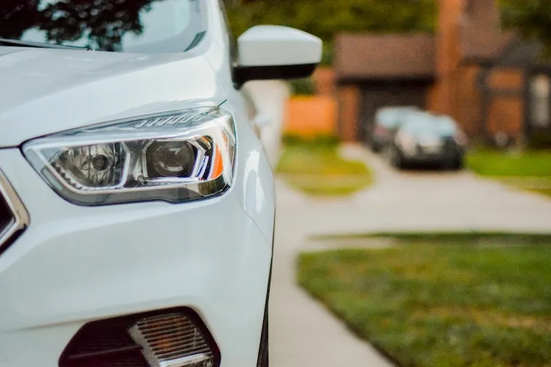 A white car parked in a driveway, with other cars visible in the background.
