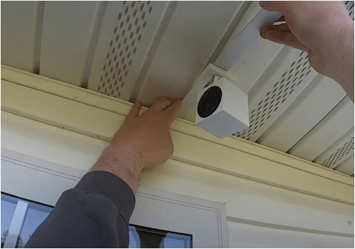 Hands mounting a small white camera under the soffit of a roof eave