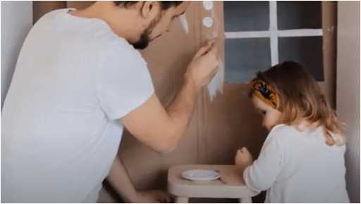 A man and a child painting a wall with white paint.