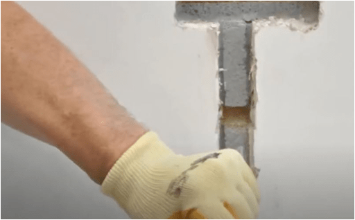 A gloved hand beside a hole cut through a wall.