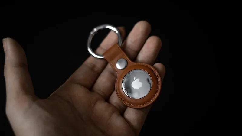 An Apple AirTag in a brown leather key ring held in an open hand