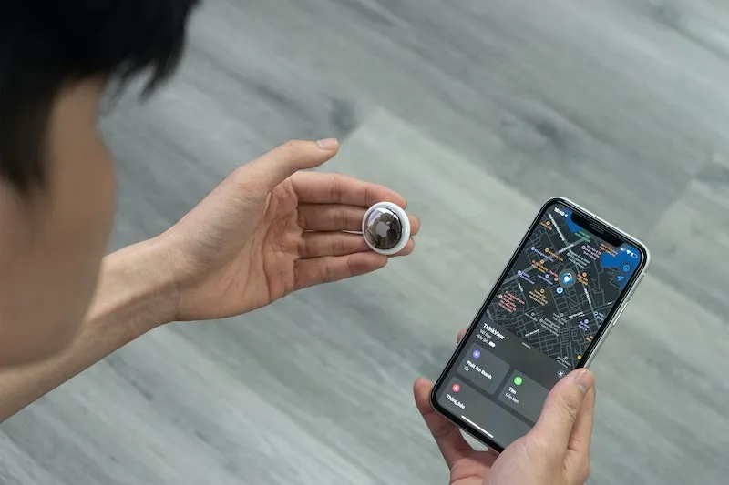 A person holding an AirTag in one hand and an iPhone showing a map in the other