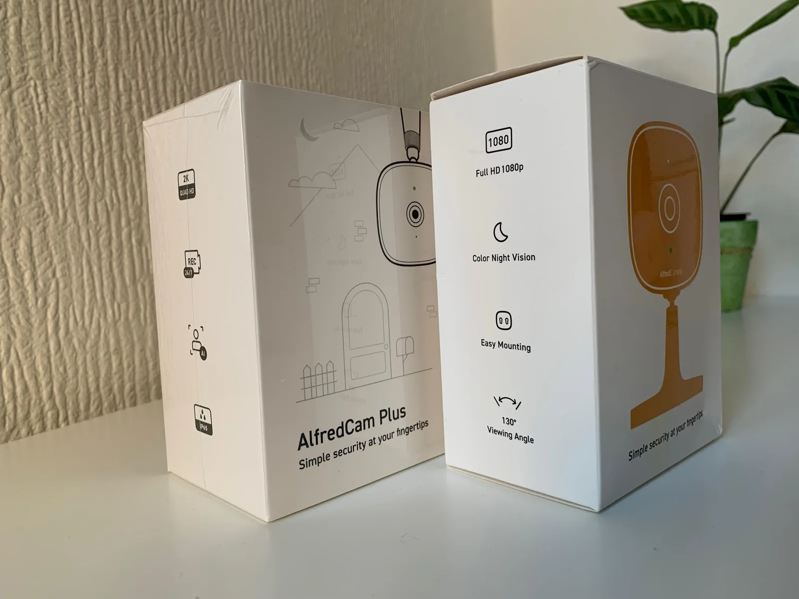 AlfredCam and AlfredCam Plus packaging put side by side on a white table.