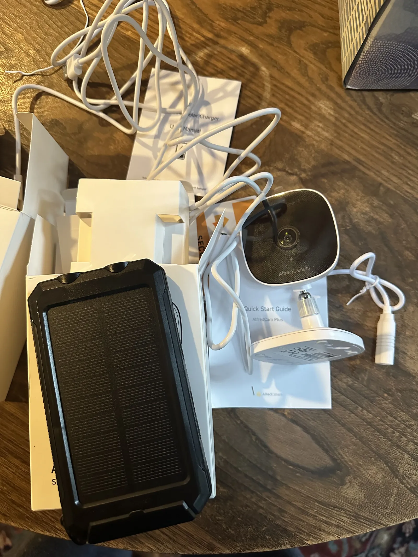 AlfredCam Plus, its quick start guide and a solar power bank on a table.