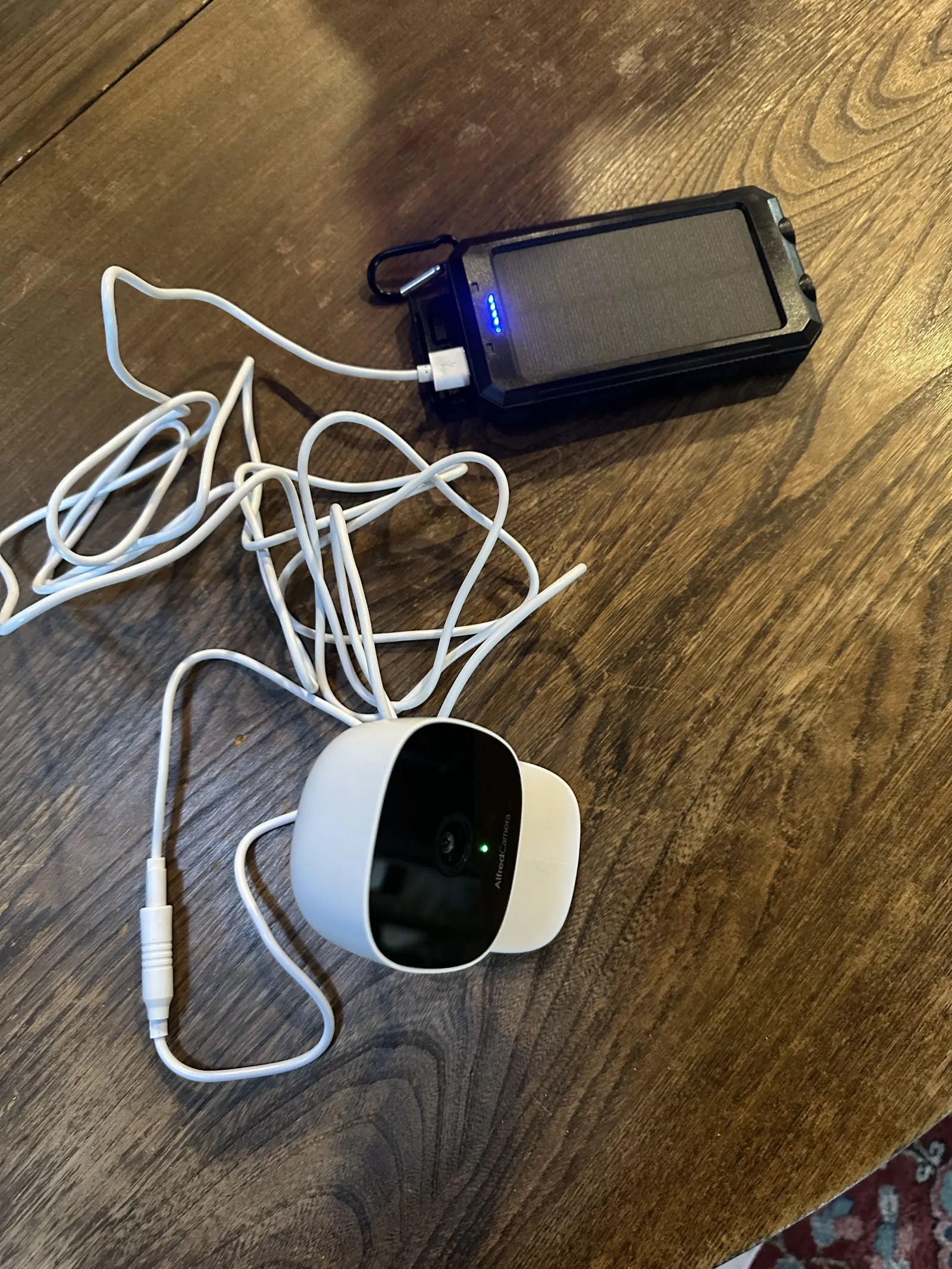 AlfredCam Plus on a wooden table connected to a solar power bank.