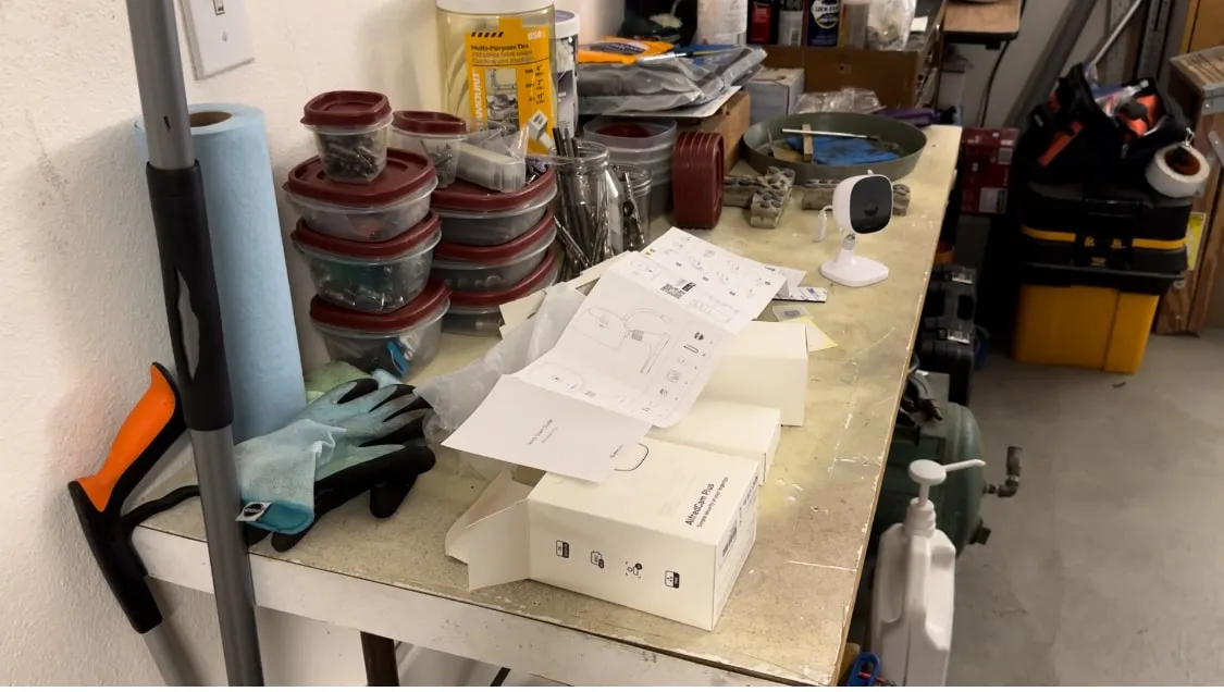 AlfredCam Plus box and setup instructions on a garage workbench, with the camera sitting on the bench.