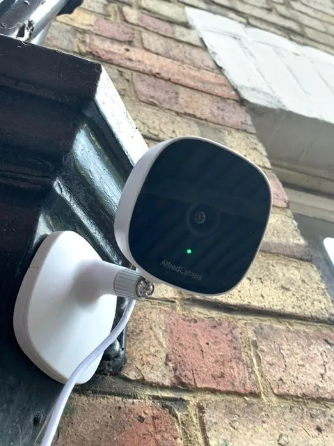 AlfredCam Plus mounted on a brick wall outside a house.