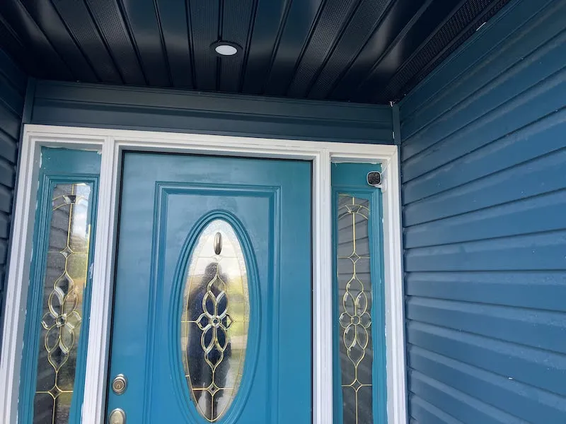 AlfredCam Plus mounted beside a teal front door on a covered porch.